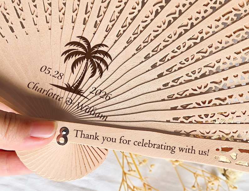May include: A wooden hand fan with a palm tree design and the text "05.28 Charlotte & William 2026" and "Thank you for celebrating with us!"