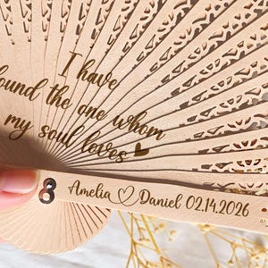 May include: A wooden hand fan with detailed cut-out patterns. The fan is engraved with the words "I have found the one whom my soul loves." It also displays the names "Amelia" and "Daniel" and the date "02.14.2026".