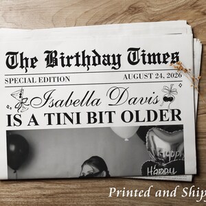 May include: A stack of newspapers with the headline "The Birthday Times" and the date August 24, 2026. The special edition newspaper is personalized for Isabella Davis, with the text "IS A TINI BIT OLDER".