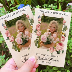 May include: A floral memorial card with a photo of a young woman holding a bouquet of pink flowers. The card reads "Forever in our hearts" and "In loving memory of Isabella Brown 1995-2025".