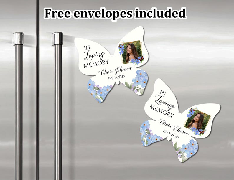 K&ouml;nnte beinhalten: Zwei wei&szlig;e, schmetterlingsf&ouml;rmige Erinnerungsmagnete mit blauen Vergissmeinnicht-Blumen. Jeder Magnet hat einen Fotorahmen und den Text "In Loving Memory" mit einem Namen und Daten. "Free envelopes included" steht oben im Bild.
