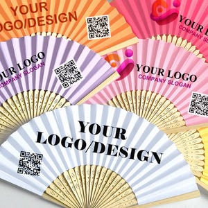 Pode incluir: Uma coleção de leques de papel abertos e coloridos com cabos de madeira. Cada leque exibe o texto "YOUR LOGO/DESIGN" ou "YOUR LOGO COMPANY SLOGAN" em negrito preto. Códigos QR também são visíveis em cada leque. Os leques são em tons de laranja, roxo, rosa, amarelo e branco.