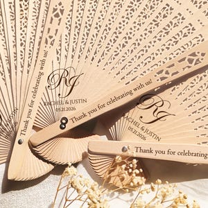 May include: Two wooden wedding fans with a lace design and the text "Thank you for celebrating with us!" and "Rachel & Justin 05.21.2026".