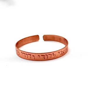 May include: A copper bracelet with Hebrew text engraved on it. The text reads "אני לדודי ודודי לי".