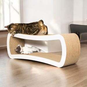 May include: Modern cat furniture with two levels. The top level features a brown tabby cat, while a gray and white cat rests on the lower level. The structure is white with a natural-colored scratching surface.