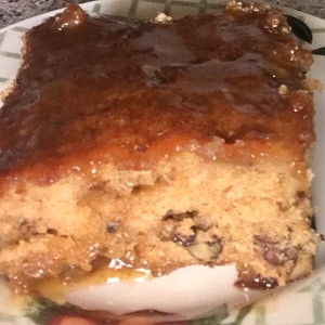 May include: A close-up of a slice of pecan cake with a brown caramel glaze. The cake is light brown and has a crumbly texture. The glaze is shiny and has a slight sheen.
