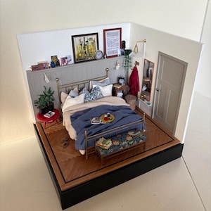 May include: A miniature dollhouse bedroom with a gold metal bed frame, blue and white bedding, a red side table, and a wooden floor. The bedroom also features a small wooden bench, a mirror, and a red coat hanging on a hook.