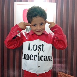 May include: A red and white leather jacket with the text "Lost Americana" in black. The jacket has a red collar and sleeves, with a white front panel. The jacket is buttoned up and worn by a person.