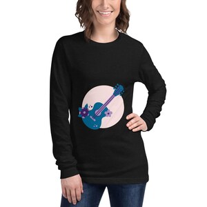 以下が含まれることがあります： 漫画のギターデザインが特徴の黒い長袖シャツ。ギターは青色で、紫色のアクセントと花のディテールがあり、薄いピンク色の円が背景にあります。楽しくてカラフルなグラフィックTシャツです。