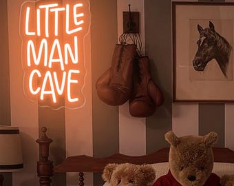 Op de afbeelding: Een slaapkamer met een bed, een neonbord met de tekst "Little Man Cave" en verschillende teddyberen. De muur is gestreept in grijs en wit.