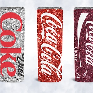 May include: Three stainless steel tumblers with glitter finishes and Coca-Cola branding. The tumblers are silver, red, and burgundy with the text "Diet Coke", "Coca-Cola", and "Coca-Cola Cherry" respectively.