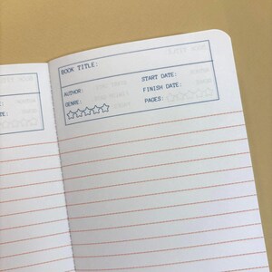 K&ouml;nnte beinhalten: Offene Notizbuchseiten mit einem Layout f&uuml;r Buchbesprechungen. Der obere Bereich hat ein blaues Feld mit den Worten "BOOK TITLE:" und andere Felder f&uuml;r "AUTHOR:" und "GENRE:" mit Sternebewertungen. Die Seiten haben rote horizontale Linien.