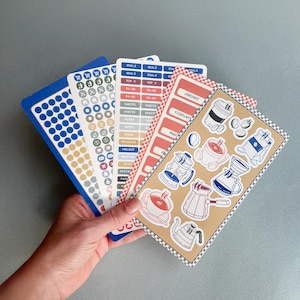 May include: A set of five rectangular sticker sheets featuring various designs including blue and tan circular dots, small icons, rectangular labels with text like GOALS and HABITS, and coffee-themed illustrations such as mugs and pots.