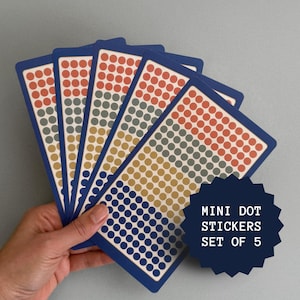 Peut inclure: Un ensemble de cinq feuilles rectangulaires d'autocollants à petits points, chacune présentant des rangées de petits cercles orange, gris, jaunes et bleus. Une étiquette bleu foncé en forme d'étoile affiche le texte MINI DOT STICKERS SET OF 5.