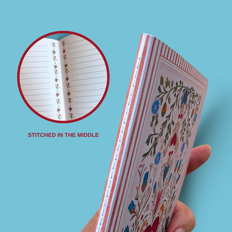 May include: A floral patterned notebook with a cream background and red, blue, and green accents. The notebook is stitched in the middle and has lined pages. The cover features a detailed floral design. The text "STITCHED IN THE MIDDLE" is visible.