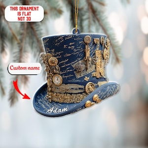 May include: A navy blue steampunk top hat ornament with gold embellishments, including gears, keys, and a clock. The hat has a brim and is decorated with script and the name "Adam". The text on the ornament reads "This ornament is flat not 3D".
