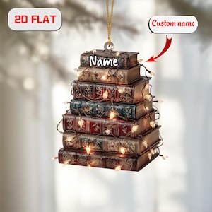 May include: A 2D flat ornament shaped like a stack of books, with the word "Name" on the top book. The books are various colours, including brown, red, and green, and are decorated with gold accents. A string of lights is wrapped around the books.