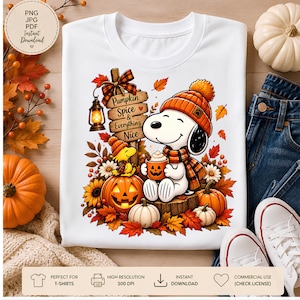 May include: A white t-shirt featuring a graphic of a white dog wearing an orange knit hat and plaid scarf, holding a pumpkin mug. Beside the dog is a yellow bird, a wooden sign reading Pumpkin Spice & Everything Nice, a lantern, and pumpkins.