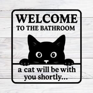 Può includere: Cartello da bagno in bianco e nero con un gatto. Il cartello recita "WELCOME TO THE BATHROOM" sopra una grafica di gatto nero e "a cat will be with you shortly..." sotto.