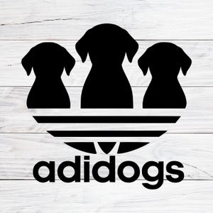 Puede incluir: Gráfico negro con tres siluetas de perros sobre un diseño estilizado con tres líneas horizontales. La palabra "adidogs" está impresa en negrita, con una fuente sans-serif debajo. El fondo es un patrón de vetas de madera clara.