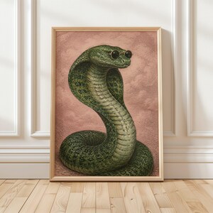 May include: A framed wall art print featuring a green cobra snake with dark scales and a light-coloured underbelly. The snake is wearing small, round, black-rimmed sunglasses. The background is a textured, dusty rose pink colour with a cloudy effect.