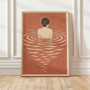 Op de afbeelding: Een ingelijste rechthoekige kunstprint met een terracotta-kleurige achtergrond. De illustratie toont een persoon met donker haar in een knot, van achteren gezien, ondergedompeld in water. Concentrische rimpelingen en lichtgekleurde reflecties lopen naar beneden.