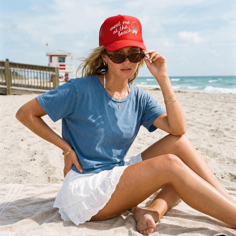 Girl wearing red hat on beach that says "meet me at the beach" in white puff print in script design
