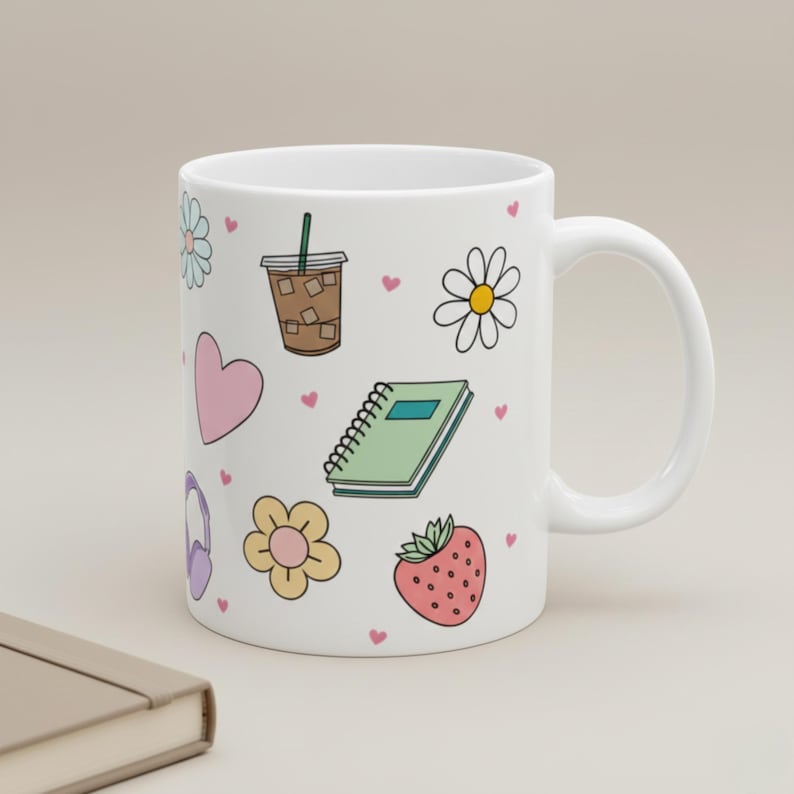 White mug with pastel hand-drawn doodles of an iced coffee, heart, journal, flower, strawberry, and tiny hearts on a desk with scattered mini hearts christian mug