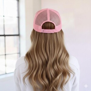 May include: A light pink trucker hat featuring a mesh back panel and an adjustable plastic snapback closure. The cap is constructed with a structured crown and a breathable mesh design, showcasing a solid pink color throughout the entire piece.