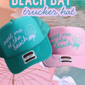 Op de afbeelding: Turquoise en roze truckerpetten met de tekst "meet me at the beach" en een schelpgrafiek. De afbeelding toont ook twee vrouwen in badpakken en zonnebrillen, en de tekst "BEACH DAY trucker hat".