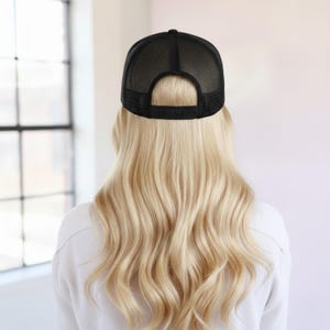 May include: A black trucker cap featuring a mesh back panel and an adjustable plastic snapback closure. The cap is constructed with a solid front panel and a breathable mesh rear section, designed with a classic structured crown and a curved brim.