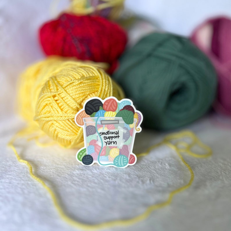 May include: A sticker of a bucket filled with colorful yarn balls. The sticker says "Emotional Support Yarn".