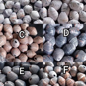 May include: Assortment of six different styles of paper beads. The beads are all oval shaped and have a spiral pattern. The beads are in various colours, including white, brown, black, and grey.