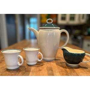 May include: A set of cream-colored ceramic coffee and tea service with green trim. The set includes a coffee pot, a creamer, and two cups.