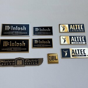 Peut inclure: Collection de badges d'&eacute;quipement audio vintage, dont McIntosh, Altec Lansing, JBL et Western Electric. Les badges sont rectangulaires avec des lettrages et des motifs dor&eacute;s et noirs. Les badges McIntosh indiquent "Legendary Performance".