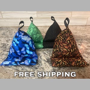May include: Four fabric phone stands in a row. One is blue with butterfly patterns, another is green with a pattern, a third is black, and the last is brown with a leaf design. Each stand has a black loop at the top.