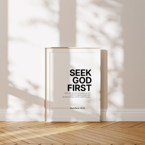 Puede incluir: Una impresi&oacute;n de arte de pared imprimible en blanco y negro con el texto "SEEK GOD FIRST" y un vers&iacute;culo b&iacute;blico de Mateo 6:33. La impresi&oacute;n est&aacute; enmarcada en un marco dorado y se muestra en un suelo de madera.