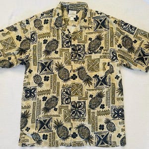 May include: Short-sleeved button-down shirt with a repeating pattern of pineapples, geometric shapes, and floral designs in shades of beige, black, and olive green. The shirt has a collared neckline and a relaxed fit, suitable for casual wear.