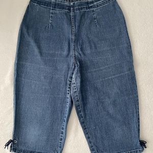 May include: Blue denim capri pants with an elastic waistband and drawstring detail at the hem. The capris have a classic five-pocket design and are made of a medium-wash denim fabric.