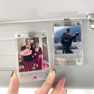May include: Two clear acrylic car visor photo clips, each holding a photograph. One shows a family in matching pajamas, the other a couple. Text on the clips reads "Drive Safe, We love you!" and "Drive Safe, I love you!"