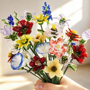 May include: A colorful bouquet of glass flowers in various shapes and colors, including red, yellow, blue, and white. The flowers are held together with green stems.