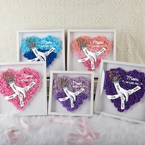 May include: Five framed heart-shaped floral arrangements in shades of blue, pink, peach, purple, and lavender. Each features a hand-holding design with the word "Mom" and personalized names. The floral hearts are set in white frames.