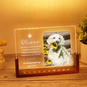 Op de afbeelding: Herdenkingsfotolijst met een foto van een hond met een zonnebloem. De lijst heeft de naam "Oliver" en een herdenkingsboodschap. De houten en acryl lijst wordt verlicht met warme lichten.