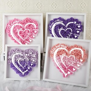 May include: Four white frames with pink and purple foam rose hearts. Each heart has a different name written inside. The names are "Sunny", "Mom", "Grandma", and "Our little world".