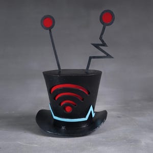 May include: A black top hat featuring a red WiFi symbol and a light blue brim. Two black antennae with red circles rise from the top. A quirky and distinctive hat.