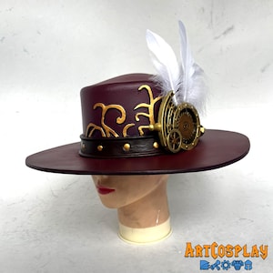 May include: A burgundy felt hat with a wide brim and a gold and brown leather band. The hat has a gold metal gear design on the side and a white feather on top.