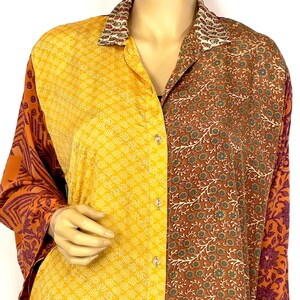 Può includere: Una camicia a maniche lunghe con bottoni realizzata in tessuto patchwork. La camicia ha uno schema di colori giallo, arancione e marrone con motivi floreali e geometrici. Il colletto è di un colore beige a contrasto.