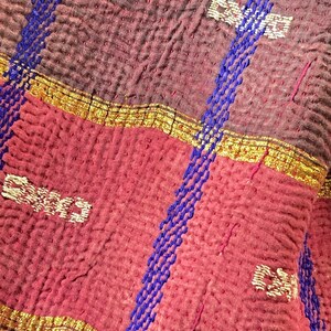 K&ouml;nnte beinhalten: Nahaufnahme einer roten und braunen Kantha-Steppdecke mit blauen und goldenen Stickereien. Die Steppdecke besteht aus mehreren Stofflagen, die zusammengen&auml;ht werden, um einen gesteppten Effekt zu erzielen. Die Stickerei ist aufwendig und detailliert, und die Farben sind leuchtend und kr&auml;ftig.