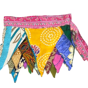 May include: A colorful patchwork skirt with a pink and green patterned waistband. The skirt is made of various fabrics and has a triangular shape.