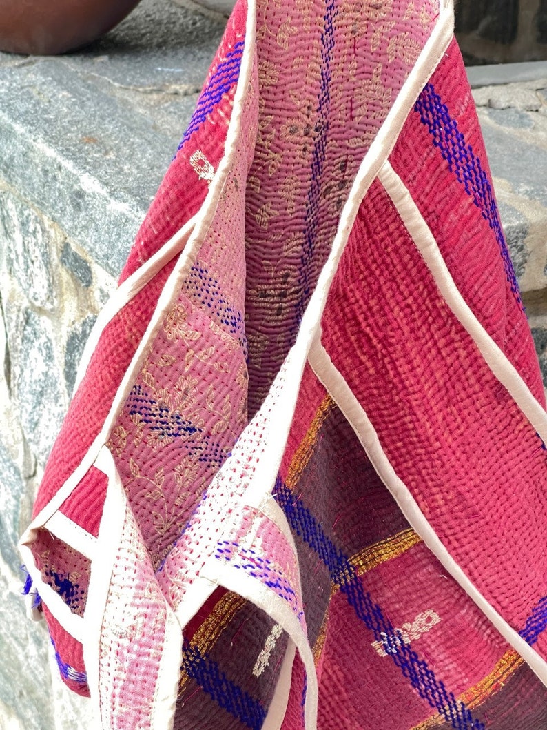 K&ouml;nnte beinhalten: Eine rosa und rote Kantha-Steppdecke-Tasche mit wei&szlig;em Besatz und blauen Stickereien. Die Tasche ist in der Mitte gefaltet und das Innere ist sichtbar.
